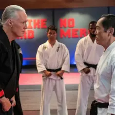 Cobra Kai obsada w strojach karate. Dwóch senseiów wpatruje się w siebie, a za nimi stoją uczniowie.