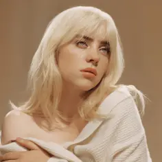 Billie Eilish z blond włosami i łzami na policzkach, w białym swetrze. Jej emocjonalne utwory poruszają serca fanów.