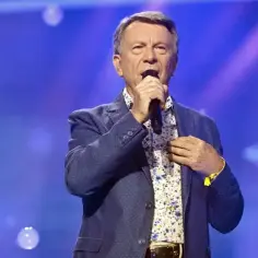 Wojciech Gąsowski śpiewa na scenie w niebieskiej marynarce w kropki i wzorzystej koszuli.