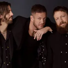 Trzech członków Imagine Dragons w czarnych strojach, gotowych na koncert.