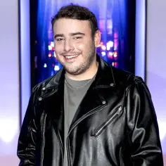 Krystian Ochman w skórzanej kurtce, uśmiechnięty. Choć na zdjęciu nie ma jego żony, jego spojrzenie sugeruje, że myśli o niej.