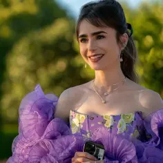 Emily w Paryżu sezon 6: Emily w spektakularnej fioletowej sukni z falbanami i kwiatowym gorsetem, trzymająca telefon.