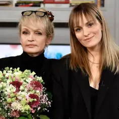 Grzegorz Wons córka, młoda kobieta z rudymi włosami, obejmuje starszą panią z blond włosami, która trzyma bukiet kwiatów.