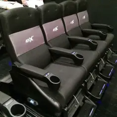 Fotele kinowe 4DX z uchwytami na napoje i podnóżkami. Czerwona lina oddziela przejście.