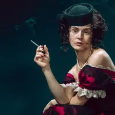 Kobieta w stylu Anny Kareniny, w eleganckiej sukni i kapeluszu z woalką, pali papierosa. Dym unosi się wokół jej twarzy.