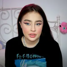 Młoda dziewczyna z niebieskimi oczami i makijażem, siedząca przed białym łóżkiem. Obok niej pluszowy pingwin i różowy Jigglypuff. Ile lat ma Fagata?
