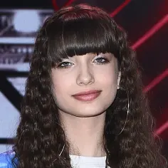 Młoda artystka z burzą loków i grzywką, znana z wiki gabor, na tle sceny.