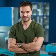 Dr. Witold w zielonym scrubie, z rękami skrzyżowanymi na piersi, w szpitalu św. Anny sezon 2.