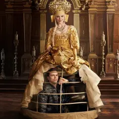 Elle Fanning w złotej sukni, z mężczyzną w klatce pod spodem. Scena z jej filmów, seriali i programów.