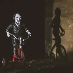Lalka Billy z Piły na czerwonym trójkołowcu, jej cień na ścianie sugeruje nadchodzący gore.