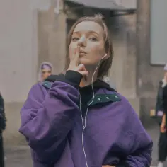 Dziewczyna w fioletowej bluzie z słuchawkami na uszach robi znak ciszy. Zastanawiasz się, ile lat ma sanah?
