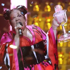 Netta z Izraela triumfuje na Eurowizji, trzymając puchar i mikrofon, podczas gdy konfetti opada na scenę.