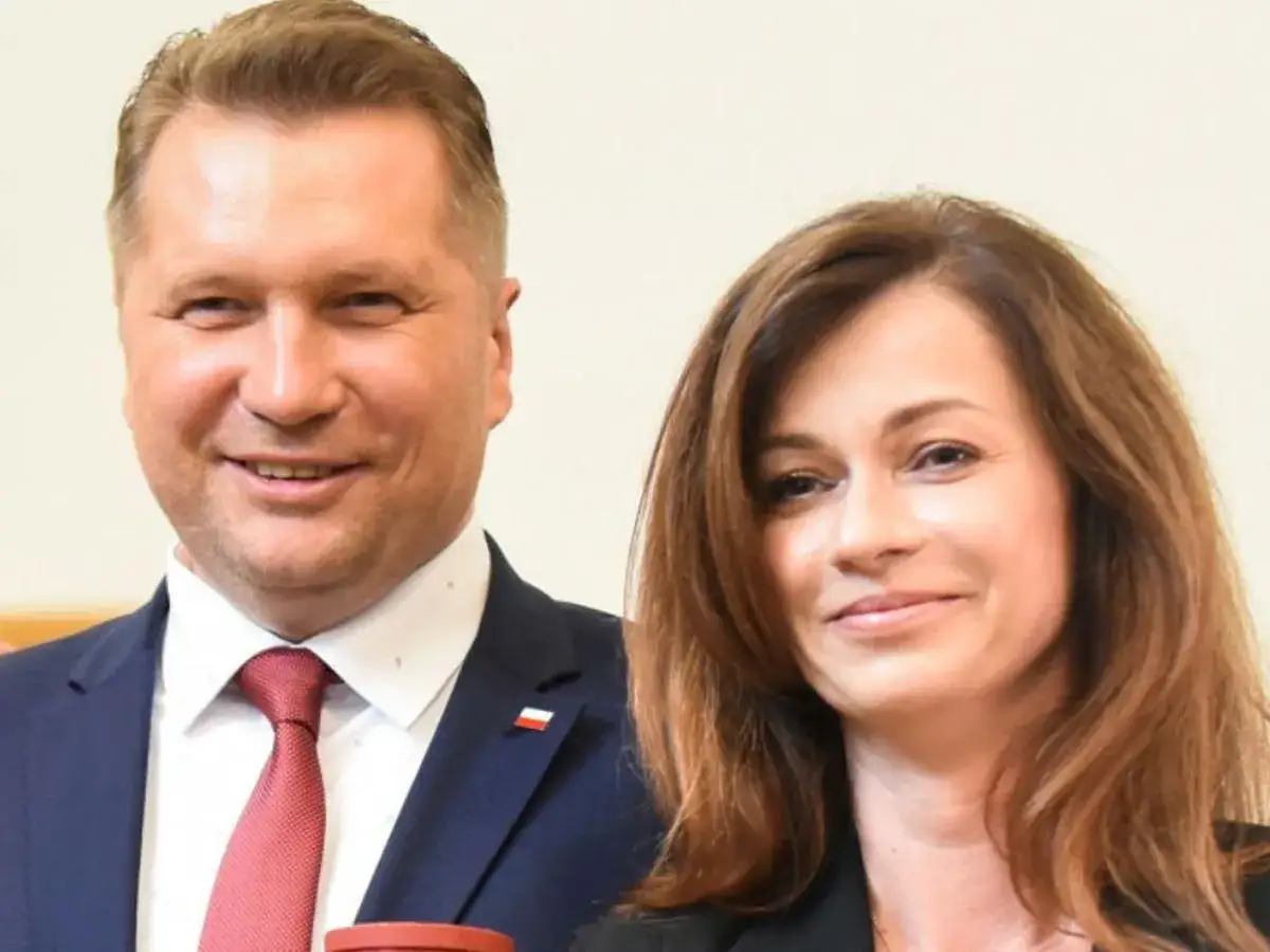 Uśmiechnięty mężczyzna w garniturze i kobieta. Katarzyna Czarnek wiek nie jest widoczny, ale oboje wyglądają na osoby w średnim wieku.