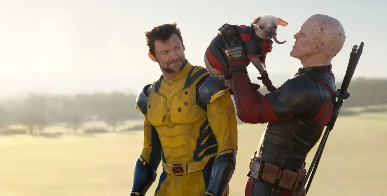 Deadpool & Wolverine obsada: Logan w żółtym kostiumie patrzy na Deadpoola, który trzyma w ramionach psa w stroju.