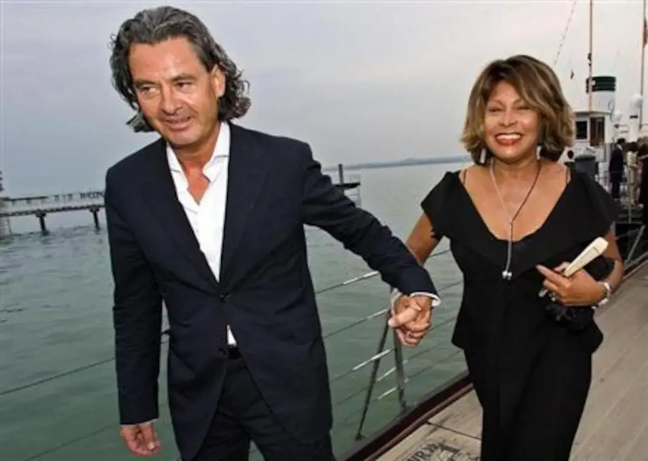 Tina Turner z mężem Erwinem Bachem trzymają się za ręce, spacerując po drewnianym molo.