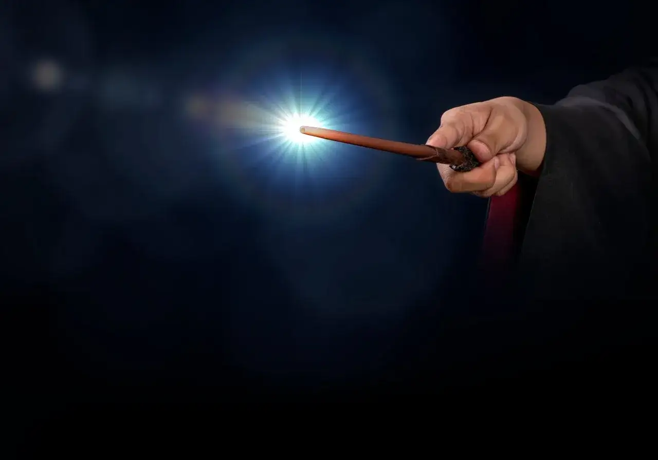 Dłoń w czarnej szacie trzyma różdżkę, z której wydobywa się oślepiające światło. To zaklęcie lumos maxima rozjaśnia mrok.
