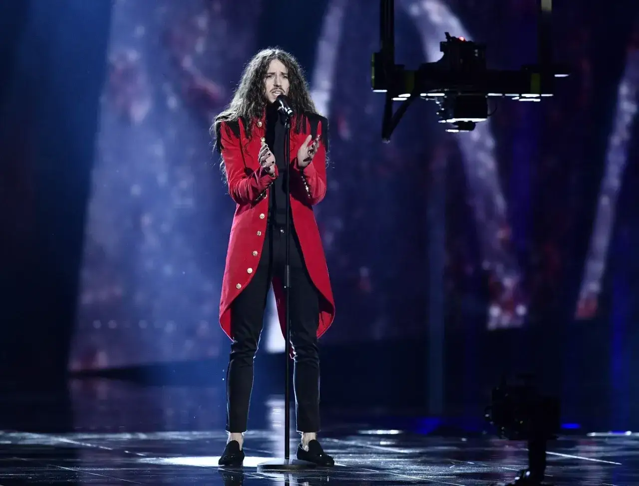 Michał Szpak na Eurowizji w czerwonym fraku, z charakterystyczną fryzurą, śpiewa na scenie.
