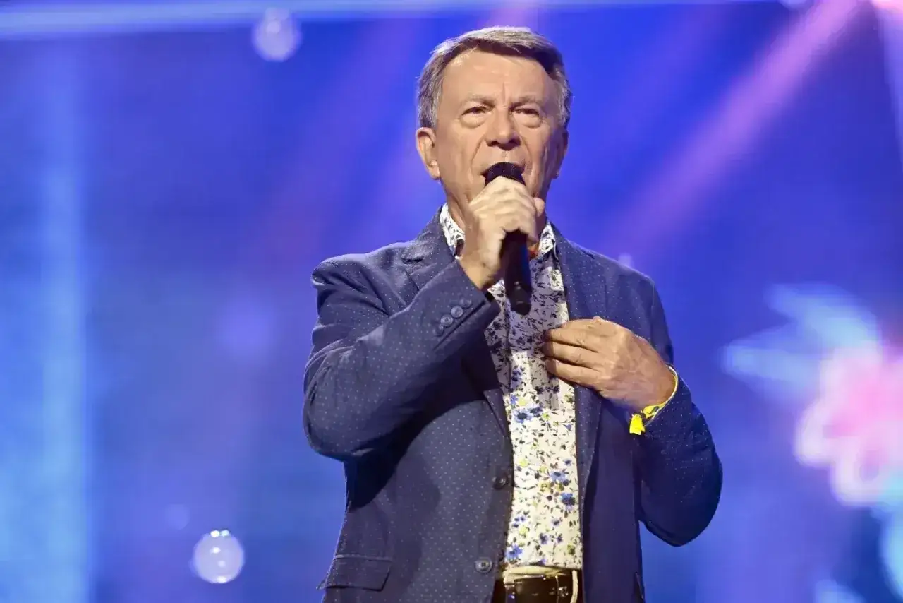 Wojciech Gąsowski w niebieskiej marynarce w kropki i kwiecistej koszuli śpiewa na scenie przy niebieskim tle.