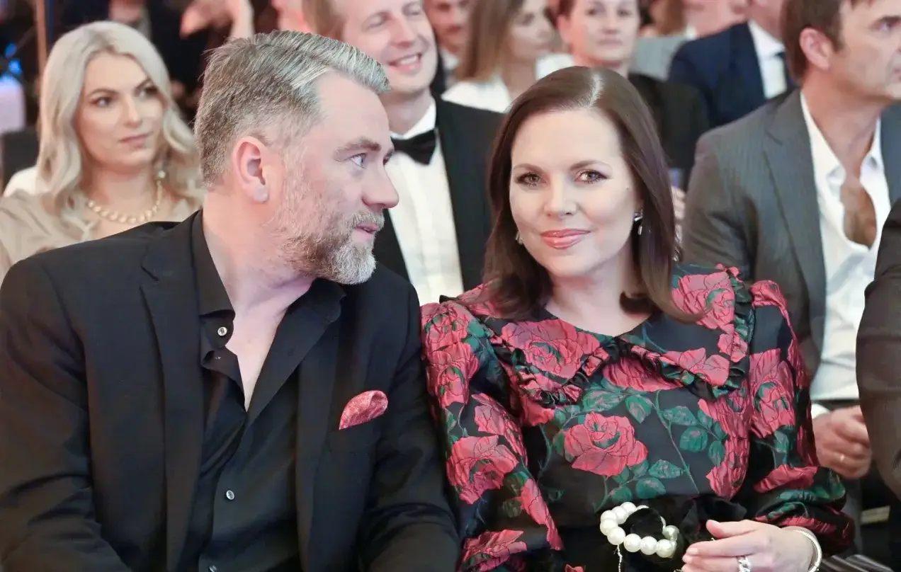 Kuba Badach z żoną, z uśmiechem patrzą na siebie. W tle widać innych gości.