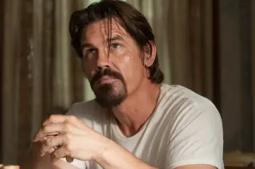 Josh Brolin w białej koszulce, z charakterystyczną brodą, wygląda jak postać z jednego z jego filmów.