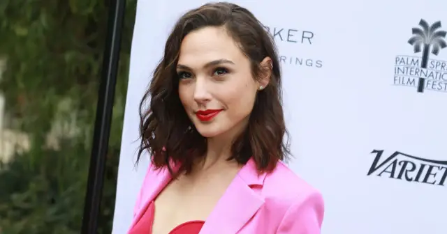 Gal Gadot w różowej marynarce i czerwonym topie, promuje swoje filmy.